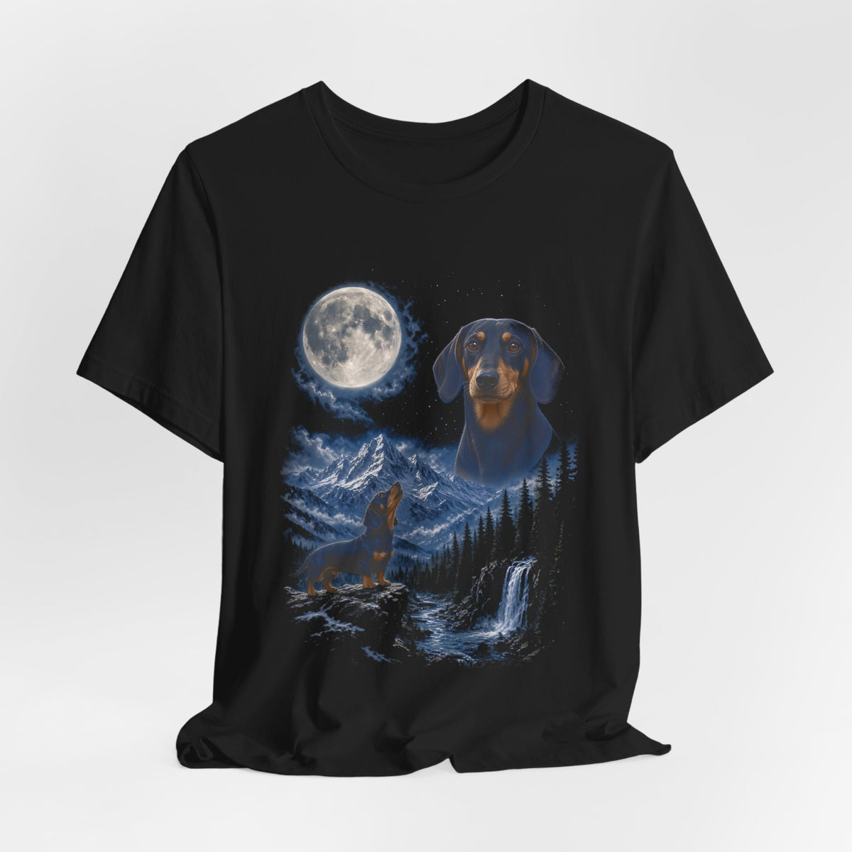 Black t-shirt with a photoreal miniature dachshund under a full moon and a second miniature dachshund howling on a cliff over mountains and a waterfall, flat lay