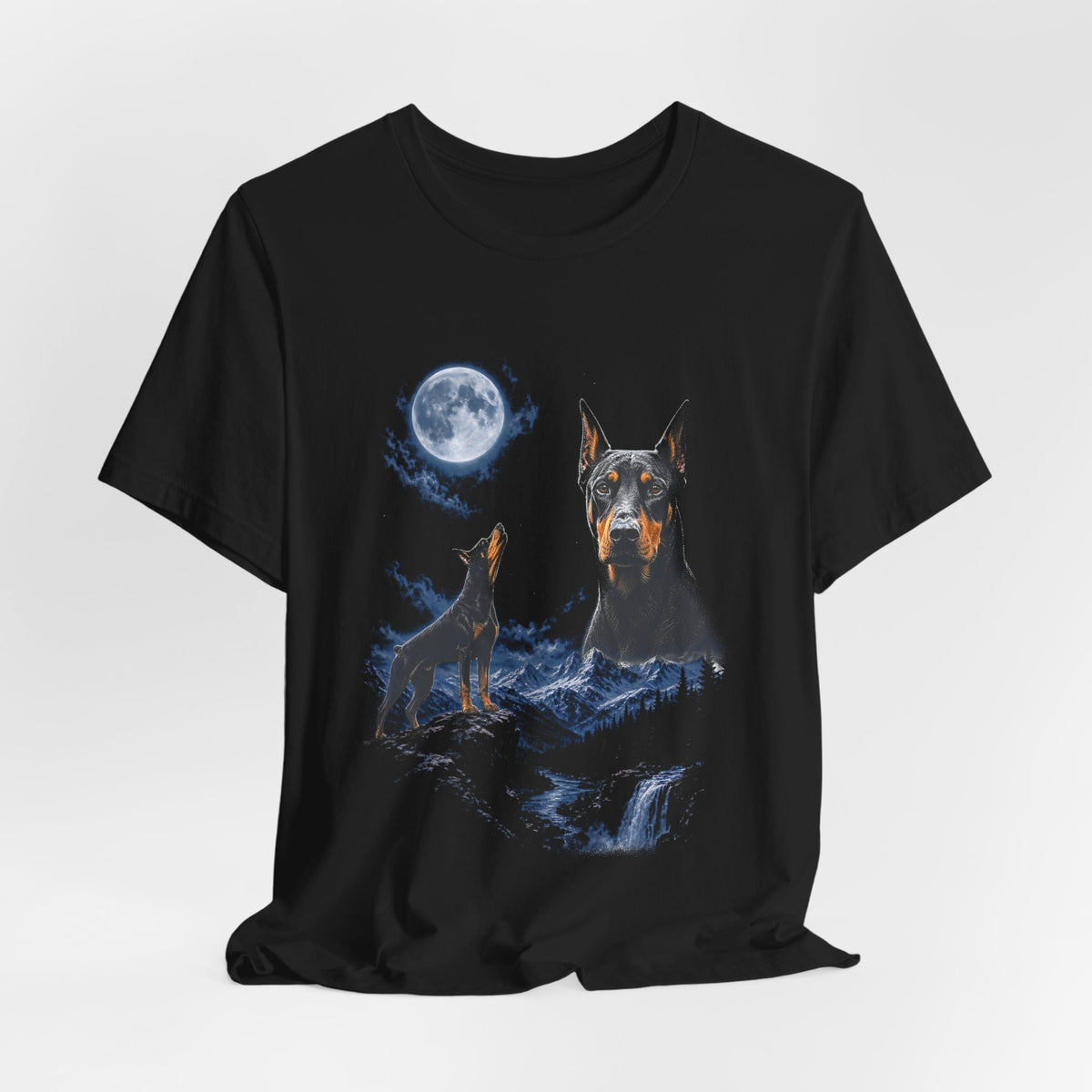 Black t-shirt with a photoreal Doberman under a full moon and a second Doberman howling on a cliff over mountains and a waterfall, flat lay